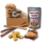 Subscription box holding 2 cute puppies and showing Duck Crisps, Bully sticks, yak cheese chews and beef kneecap